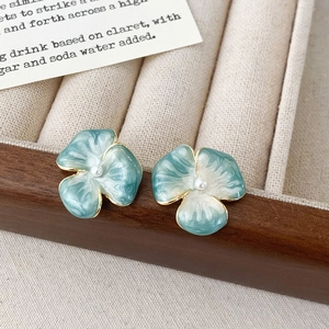 Dettaglio di orecchini a lobo a fiore blu con petali in smalto e perla in scatola di legno