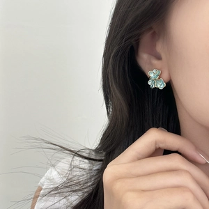 Close-up of elegant blue enamel floral stud earrings worn by a model in soft light