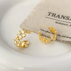 Macro detail of gold floral hoop earrings with white enamel petals on a ceramic dish