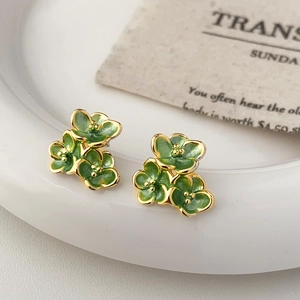 Detail of floral enamel stud earrings in green and gold on white ceramic plate