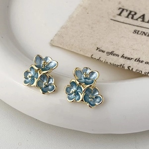 Macro detail of blue floral enamel earrings resting on a white ceramic tray with paper