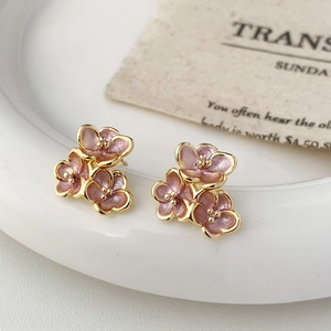 Detailed view of elegant pink floral stud earrings with gold accents on a white plate