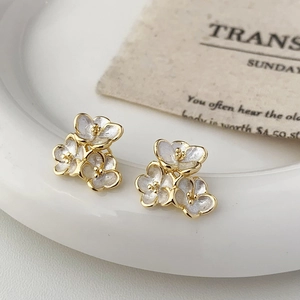 Detail of floral earrings with white enamel petals and gold accents on a vintage tray