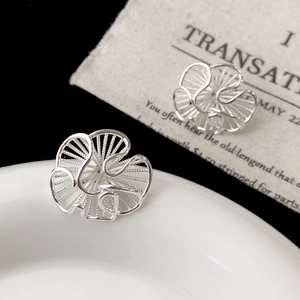 Macro detail of silver flower earrings with radiant textured hollow design on white plate