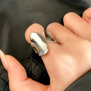 Silver asymmetric liquid metal open ring with polished finish on a woven background