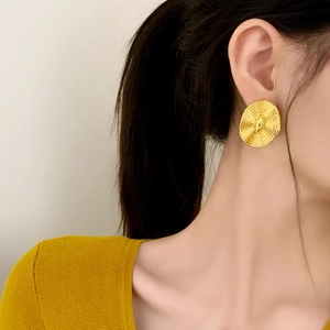 Elegant gold textured round earrings featuring a radial design on a model