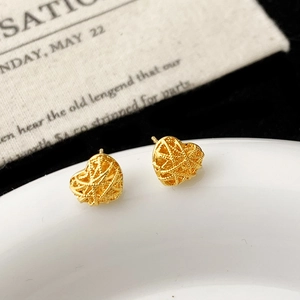 Gros plan de boucles d'oreilles cœur dorées avec un design tissé ajouré sur céramique