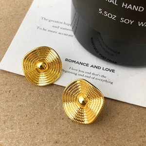 Macro detail of gold textured metal earrings with spiral pattern and central metallic bead