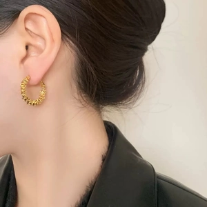 Boucle d'oreille créole dorée minimaliste à texture lave sur mannequin en veste de cuir noir