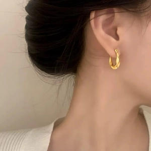 Gros plan d'élégantes créoles torsadées en or portées par un mannequin sous une lumière douce