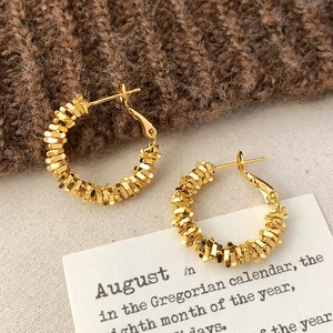 Détail macro de boucles d'oreilles créoles dorées texturées sur fond en maille douce