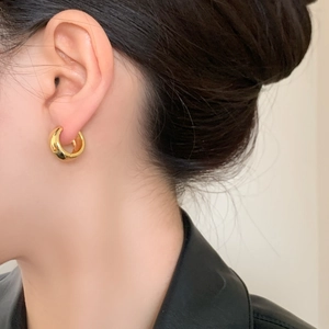 Minimalist gold geometric hoop earring for women worn by a model in a black jacket