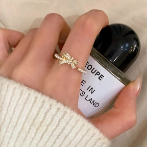 Elegant gold bow ring with pearls and zircons shown on a model hand with a perfume bottle