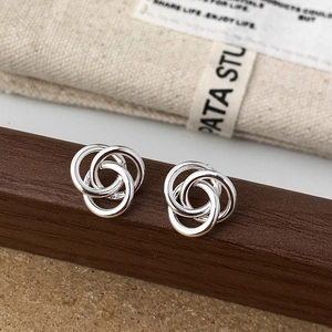 Detail of interlocking silver knot earrings showing polished texture on a wood surface