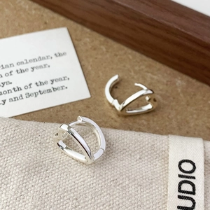 Close-up of minimalist silver hollow heart hoop earrings on a textured linen fabric