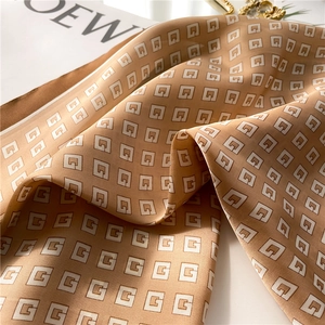 Detail of silk-like scarf with gold-brown 'G' letter pattern and satin texture