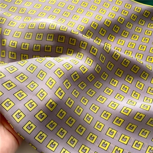 Macro detail of silk-like satin scarf featuring yellow G-letter pattern and elegant folds