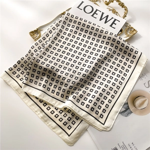 Detailed view of luxury cream silk scarf with black G pattern on golden tray