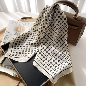 Silk square scarf with black G-geometric pattern draped over a brown leather handbag