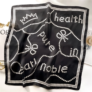 Detailed view of black polka dot silk scarf with elegant letter patterns and crown motifs