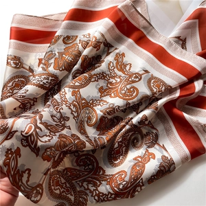 Detailed view of the soft silk-texture paisley square scarf with vibrant orange and red borders