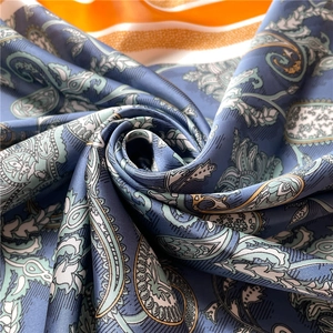 Macro detail of paisley silk scarf with blue patterns and orange striped trim design