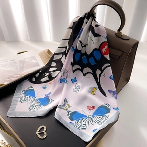 Détail du foulard en soie lilas avec motif papillon noué sur un sac à main en cuir