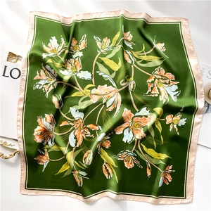 Detail of 70cm square silk scarf featuring floral lily prints and emerald green borders