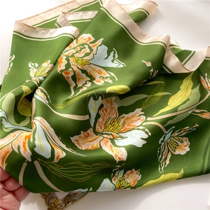 Detailed view of dark green silk square scarf featuring orange lilies and striped edges