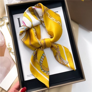 Close-up of elegant mustard yellow silk scarf with chain pattern on display tray