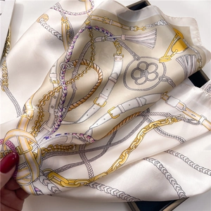 Detail of silk scarf featuring golden chain, tassel, and belt motifs on cream fabric