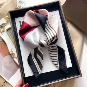 Detail of geometric stripe silk scarf folded in a brown gift box on a magazine