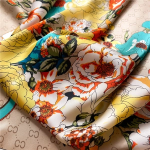 Macro shot of orange rose print silk scarf featuring interlocking letter texture and satin sheen