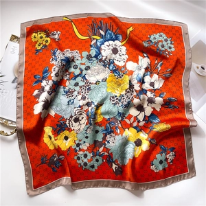 Close-up of a floral silk scarf with orange tones, monogram patterns, and deep brown edges