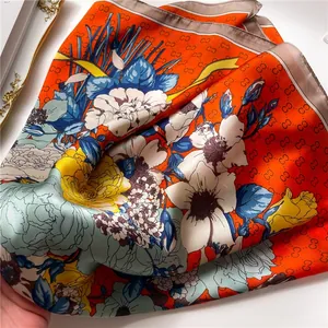 Detail of silk-like square scarf featuring orange floral print and interlocking patterns
