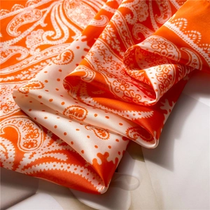 Detail of silk scarf showing orange paisley patterns and smooth satin texture finish