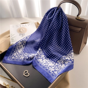 Elegant navy blue silk scarf with rose print and grid pattern draped on a handbag