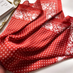 Detail of red silk-like scarf featuring white geometric patterns and floral borders