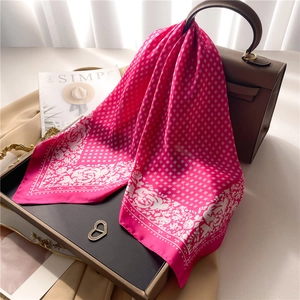 Elegant rose patterned silk scarf draped on a leather handbag with a minimalist backdrop