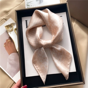 Close-up of a pink silk scarf with geometric diamond pattern in a black gift box