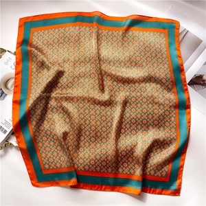 Detail of satin silk square scarf showing orange flower patterns and geometric grid texture