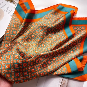 Detail of satin scarf showing orange and teal geometric floral pattern and glossy texture