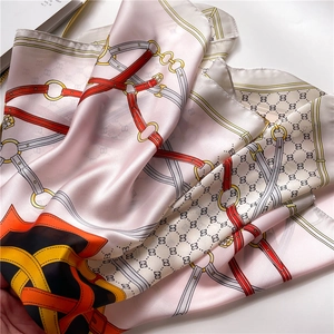 Gros plan d'un foulard en satin rose avec motifs équestres et détails d'anneaux dorés