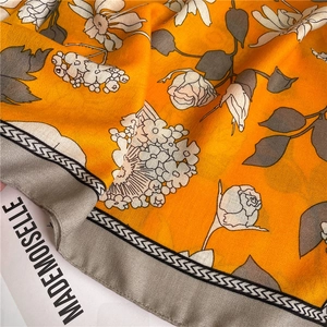 Détail d'un foulard en soie aux motifs floraux orange et bordure géométrique chic