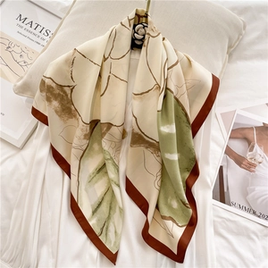 Close-up of silk square scarf with floral print and camellia brooch on white dress