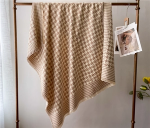 Close-up of beige houndstooth scarf with soft fringe edges hanging on a metal rack