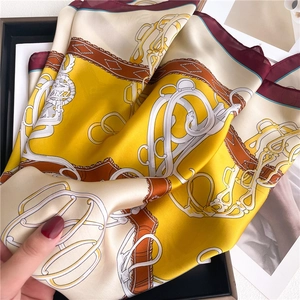 Close-up of yellow silk scarf with burgundy border and equestrian chain pattern texture