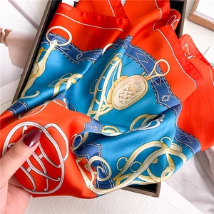 Detail of silk square scarf featuring vintage horsebit and chain patterns in orange and blue