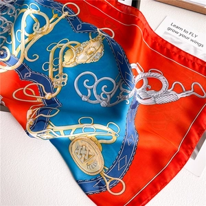 Detail of satin silk scarf with orange blue equestrian pattern and golden chains