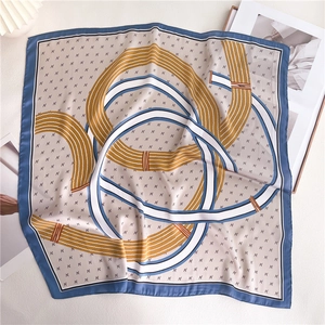 Detailed flat lay of a blue geometric 70x70cm square silk scarf on a white table